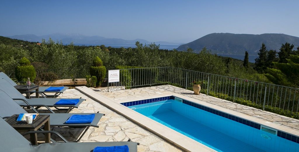 Sun loungers and pool with views from the terrave of the coastline and mountains of Kefalonia, Greek Islands